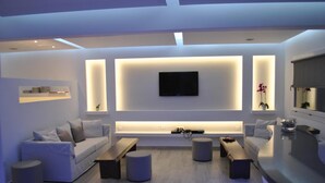 Uma sala de estar moderna com uma TV de tela plana na parede, um sofá, dois pufes e uma mesa de centro.
