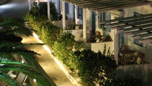 Um corredor de hotel com área de estar coberta ao ar livre, palmeiras e um caminho de pedra.