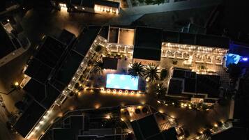 An aerial view of a hotel with a swimming pool, outdoor seating, and a well-lit patio area.