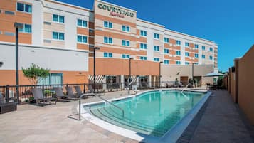 A Courtyard by Marriott hotel with a swimming pool, lounge chairs, and a clear blue sky.