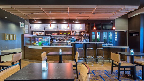 A restaurant with wooden ceiling, multiple tables, chairs, a counter with a menu, and a kitchen area. - Courtyard Columbus (Columbus)