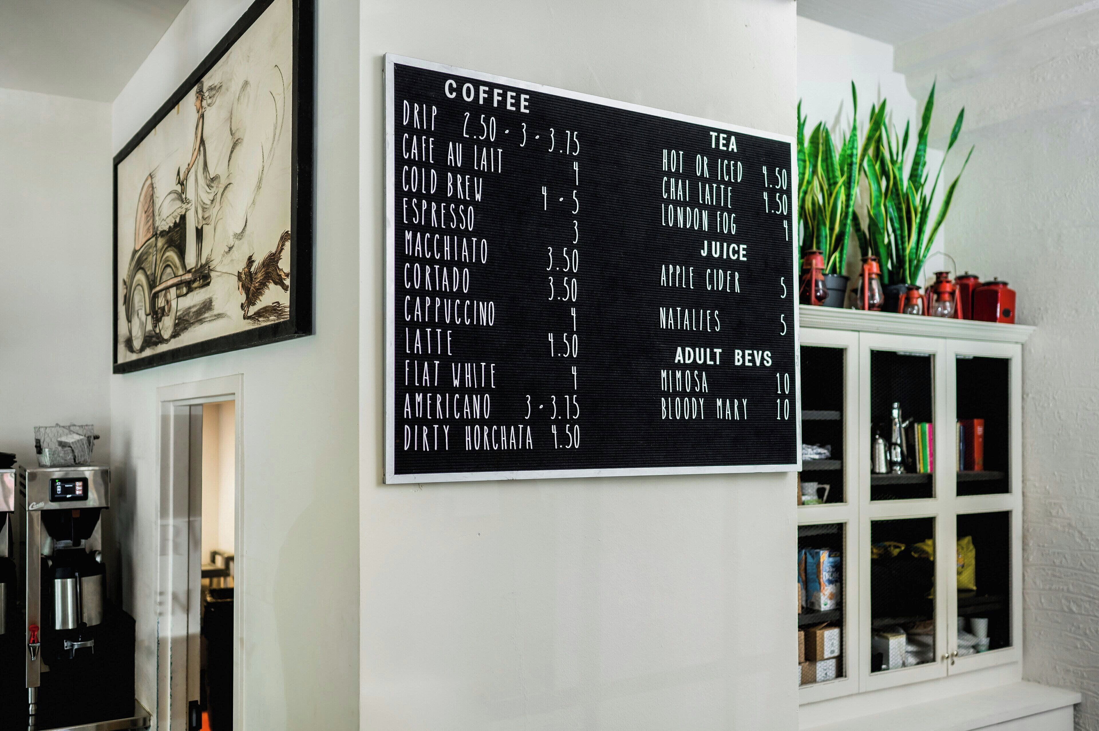 A coffee menu on a wall with a framed artwork above it.