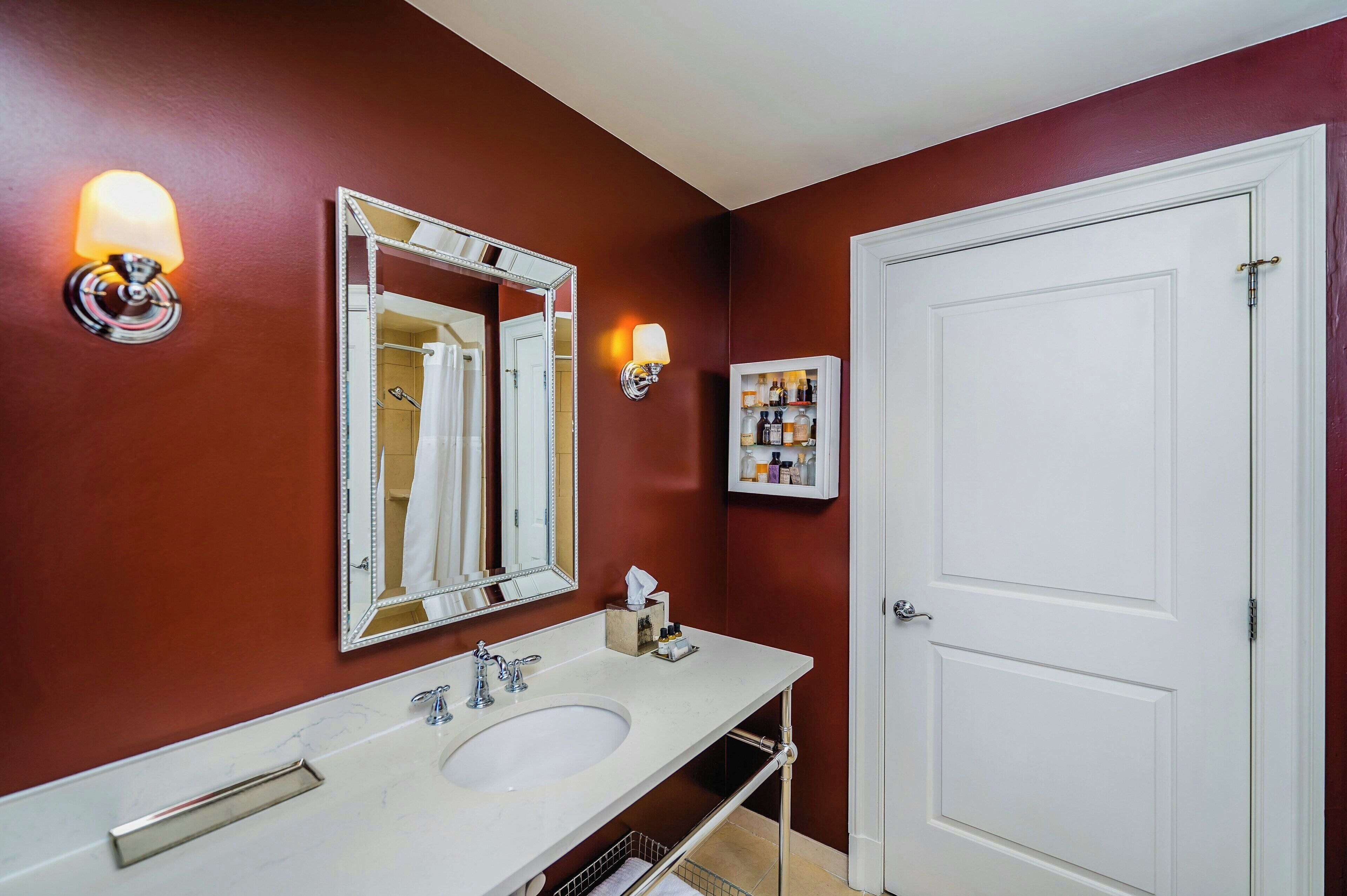 Une salle de bain avec un lavabo blanc, un grand miroir, une porte blanche et un luminaire fixé au mur.