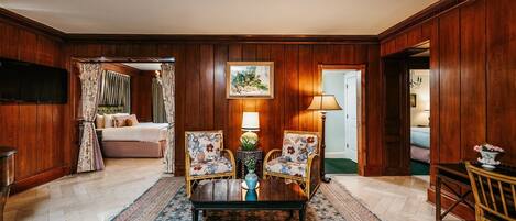 Una habitación con paneles de madera, un sofá, dos sillones, una mesa de centro, un tapete y un cuadro en la pared.