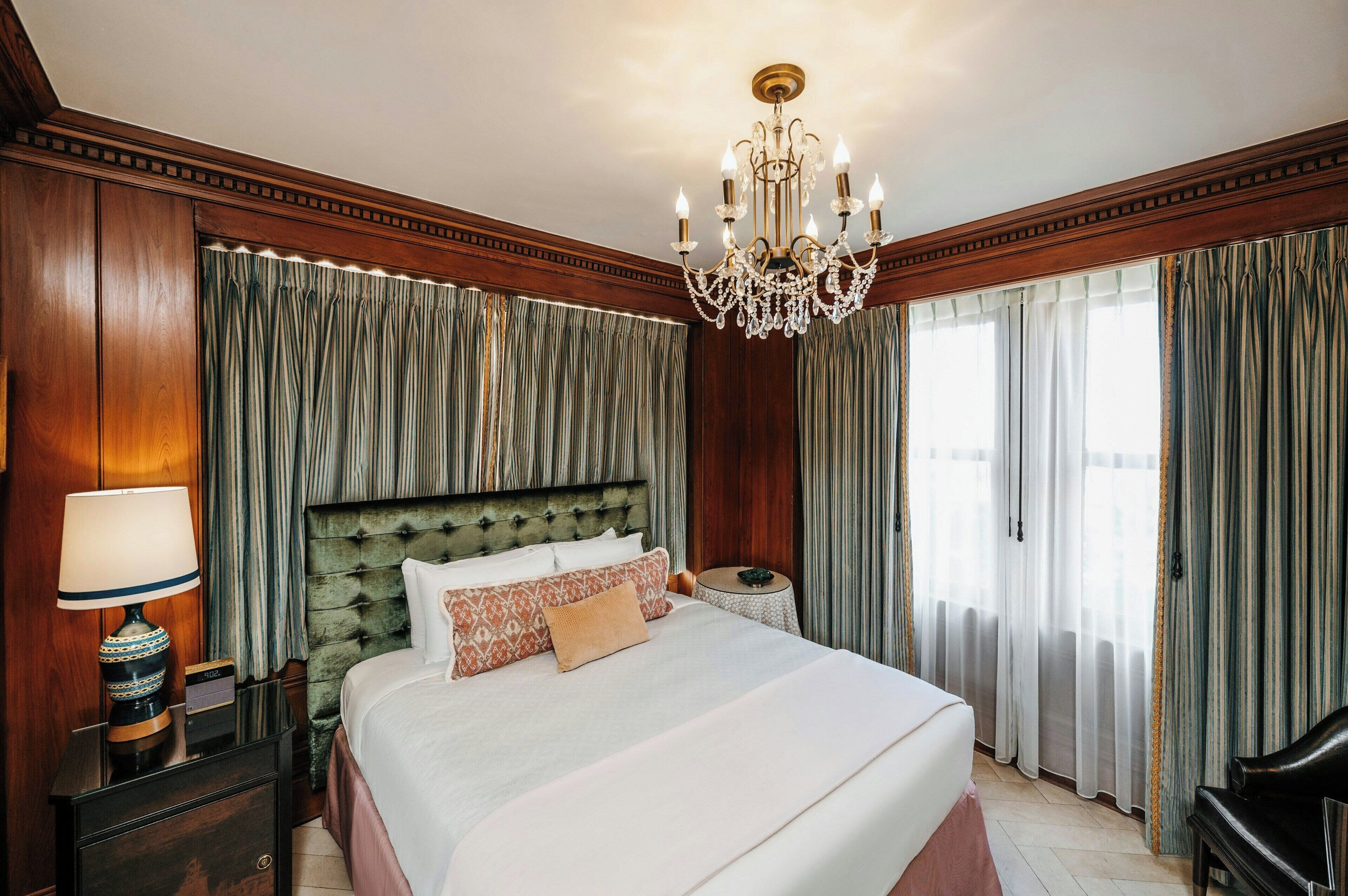 A hotel room with a large bed, a chandelier, and curtains.