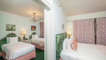 A hotel room with two beds, a chandelier, floral curtains, and artwork on the walls.