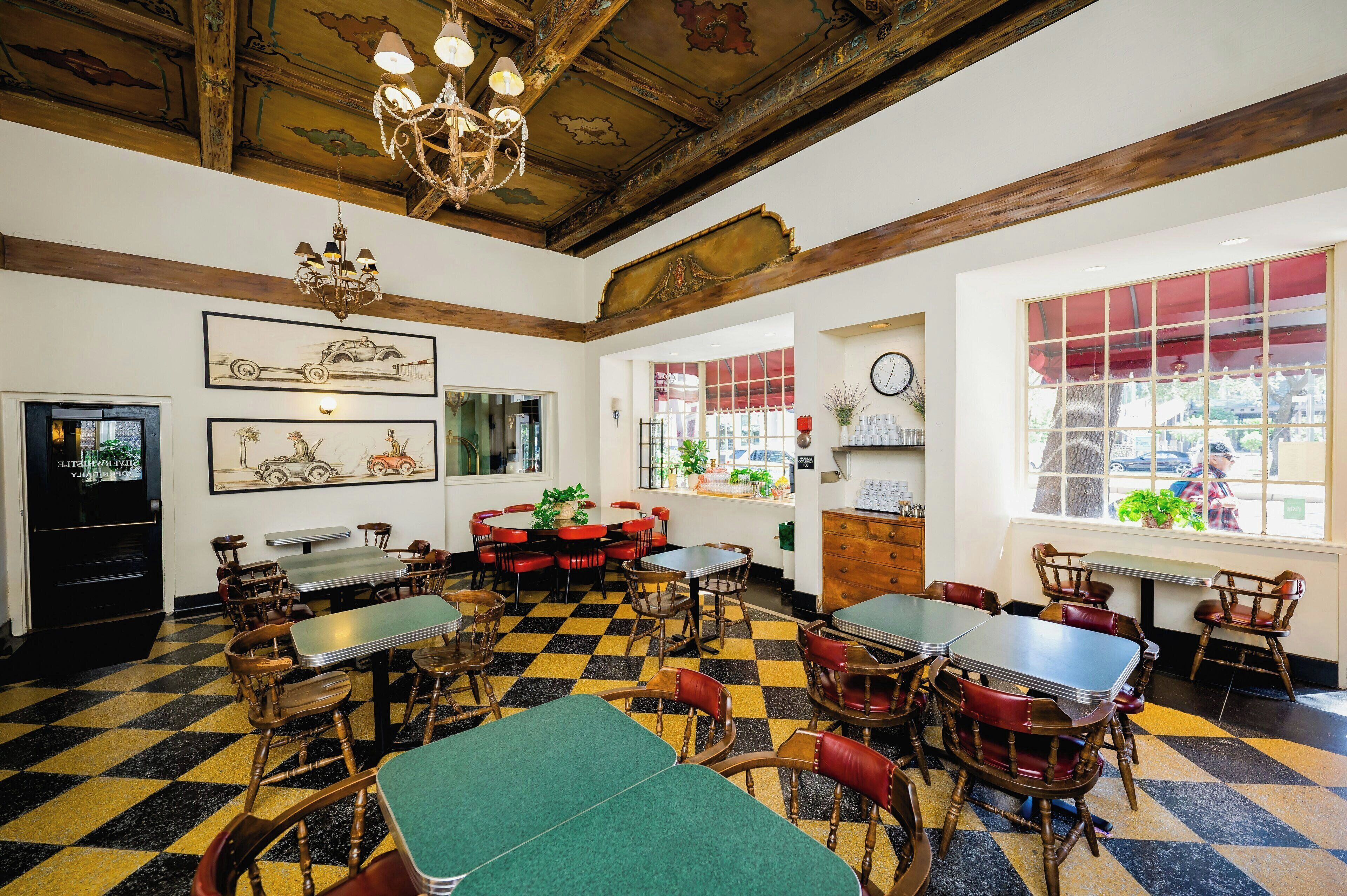 A restaurant with checkered flooring, wooden tables, and chairs, a chandelier, and artwork on the walls.