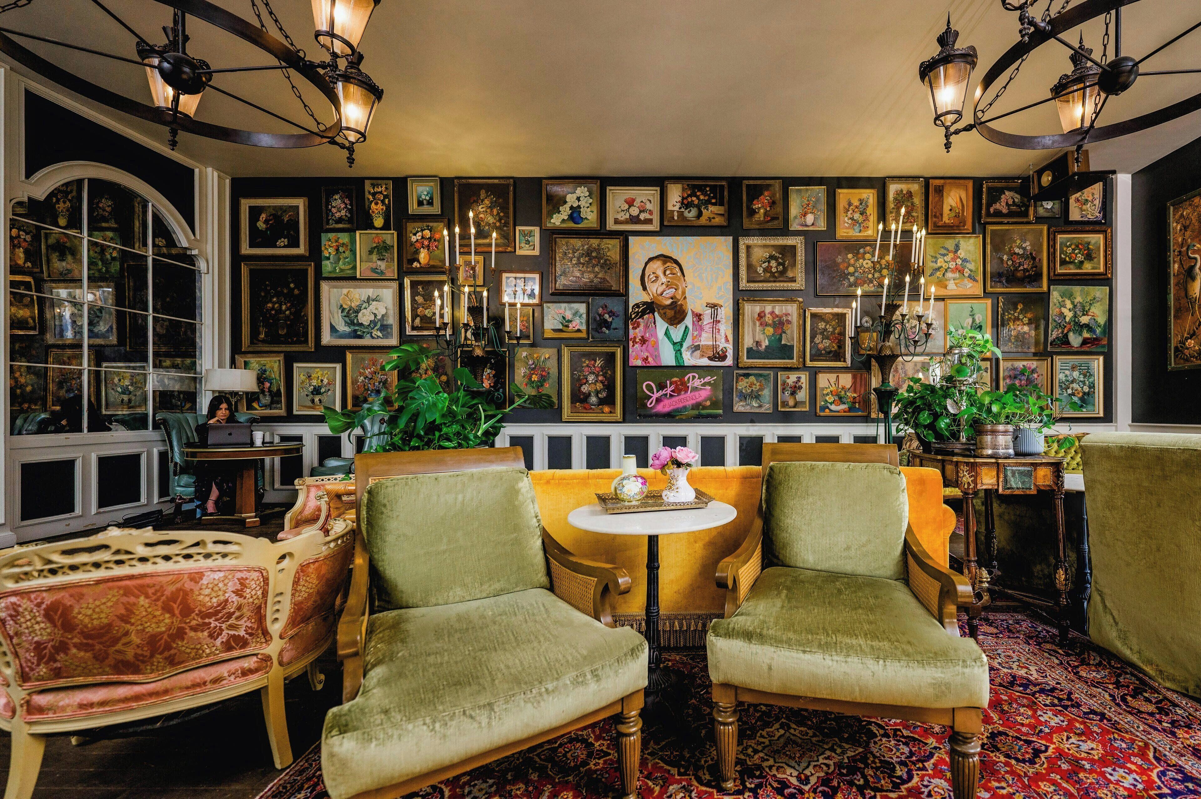 Una habitación con dos sillones verdes, una mesa redonda y una pared decorada con obras enmarcadas.