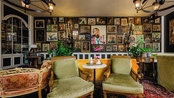 Una habitación con dos sillones verdes, una mesa redonda y una pared decorada con obras enmarcadas.