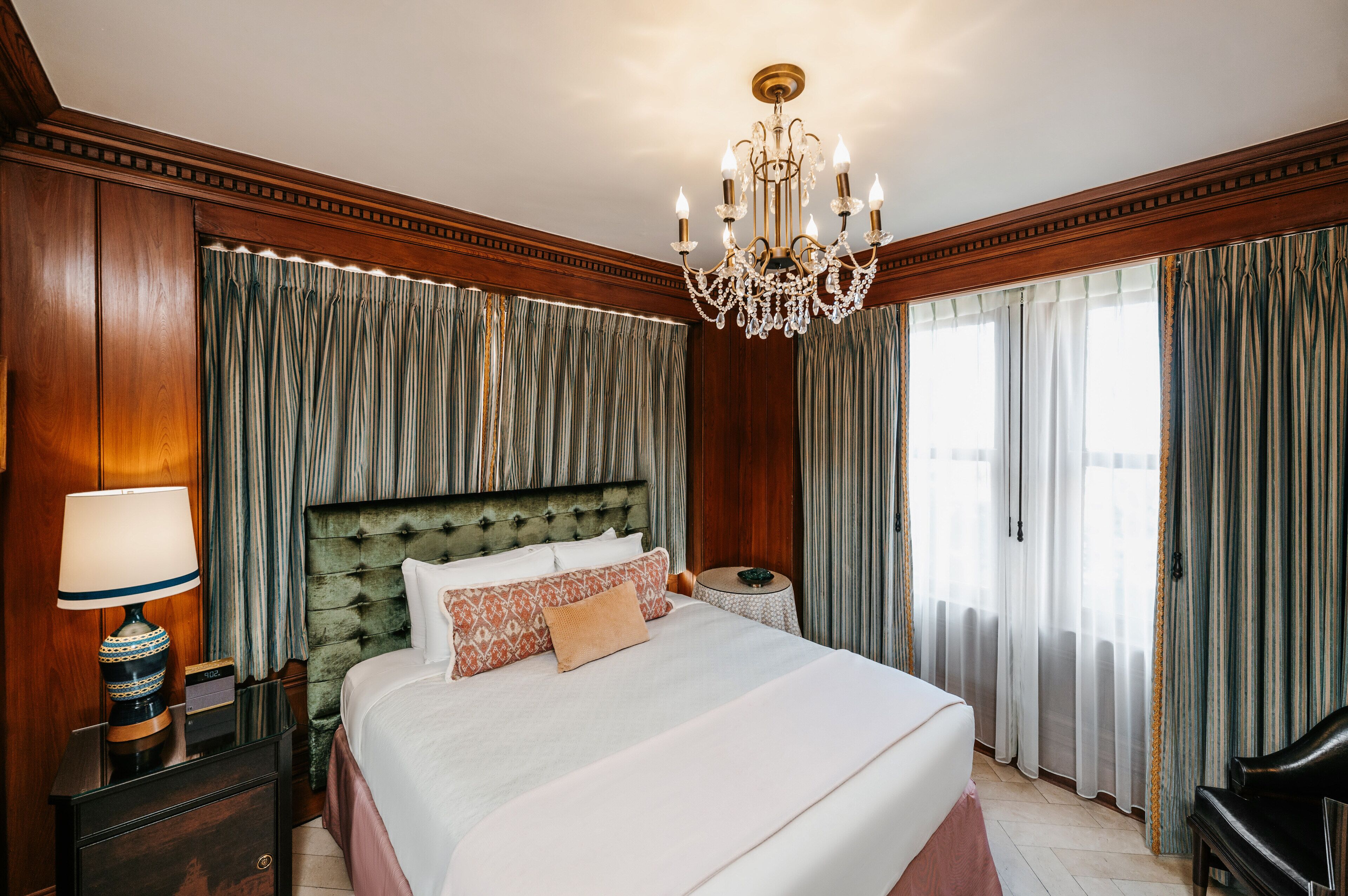 Une chambre d’hôtel avec un grand lit, un lustre, des boiseries et des rideaux.