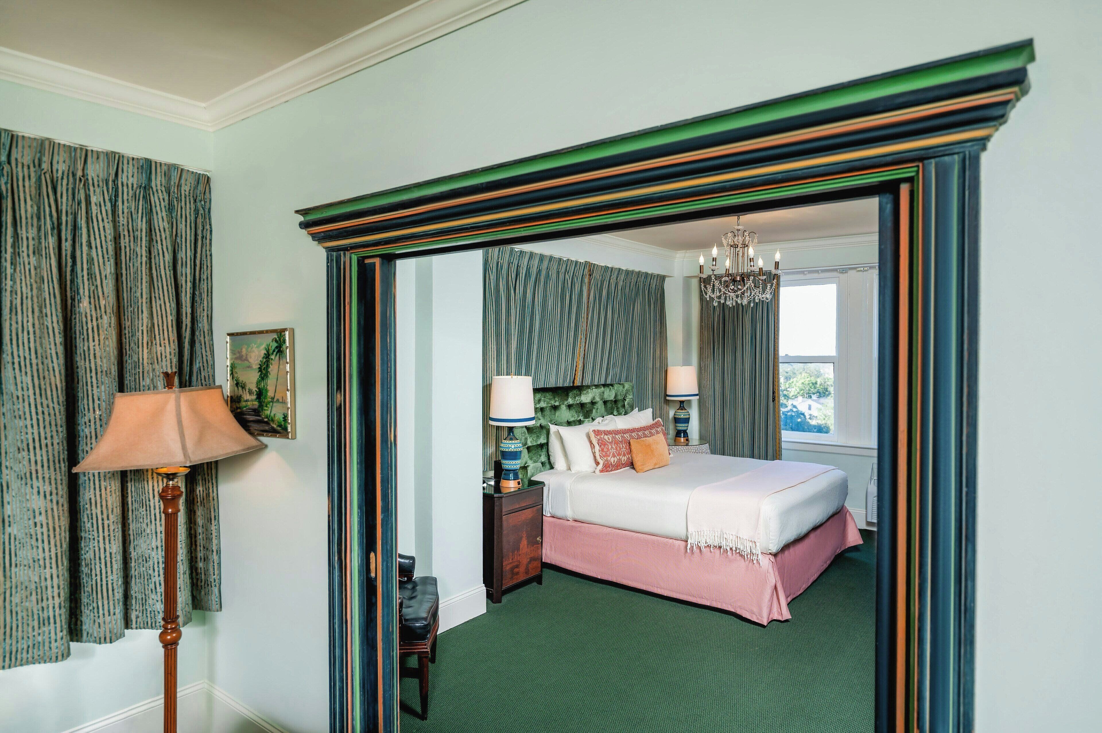 A hotel room with a bed, a nightstand, a lamp, a picture on the wall, and a window with curtains.