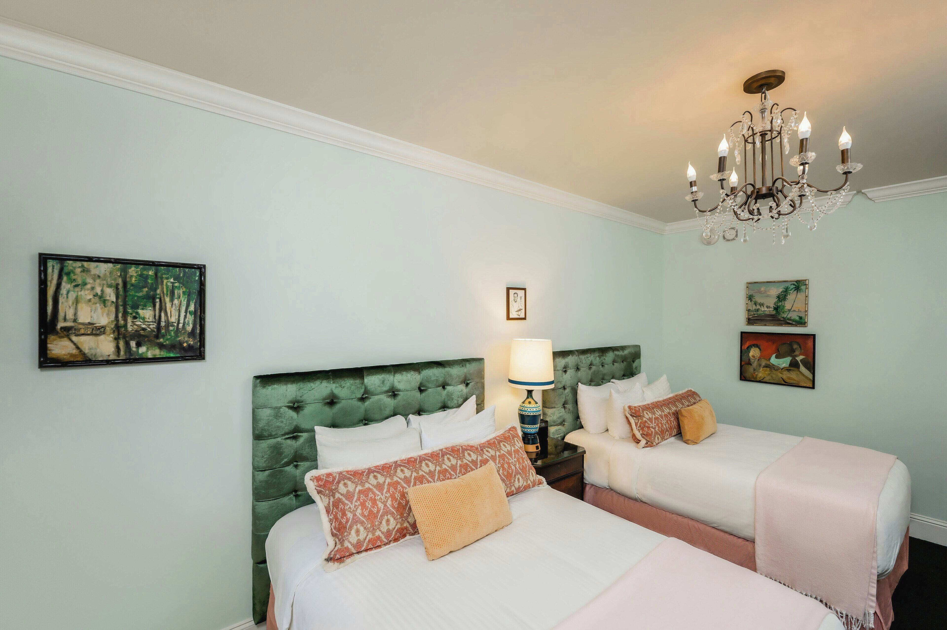 A hotel room with two beds, a chandelier, and artwork on the walls.