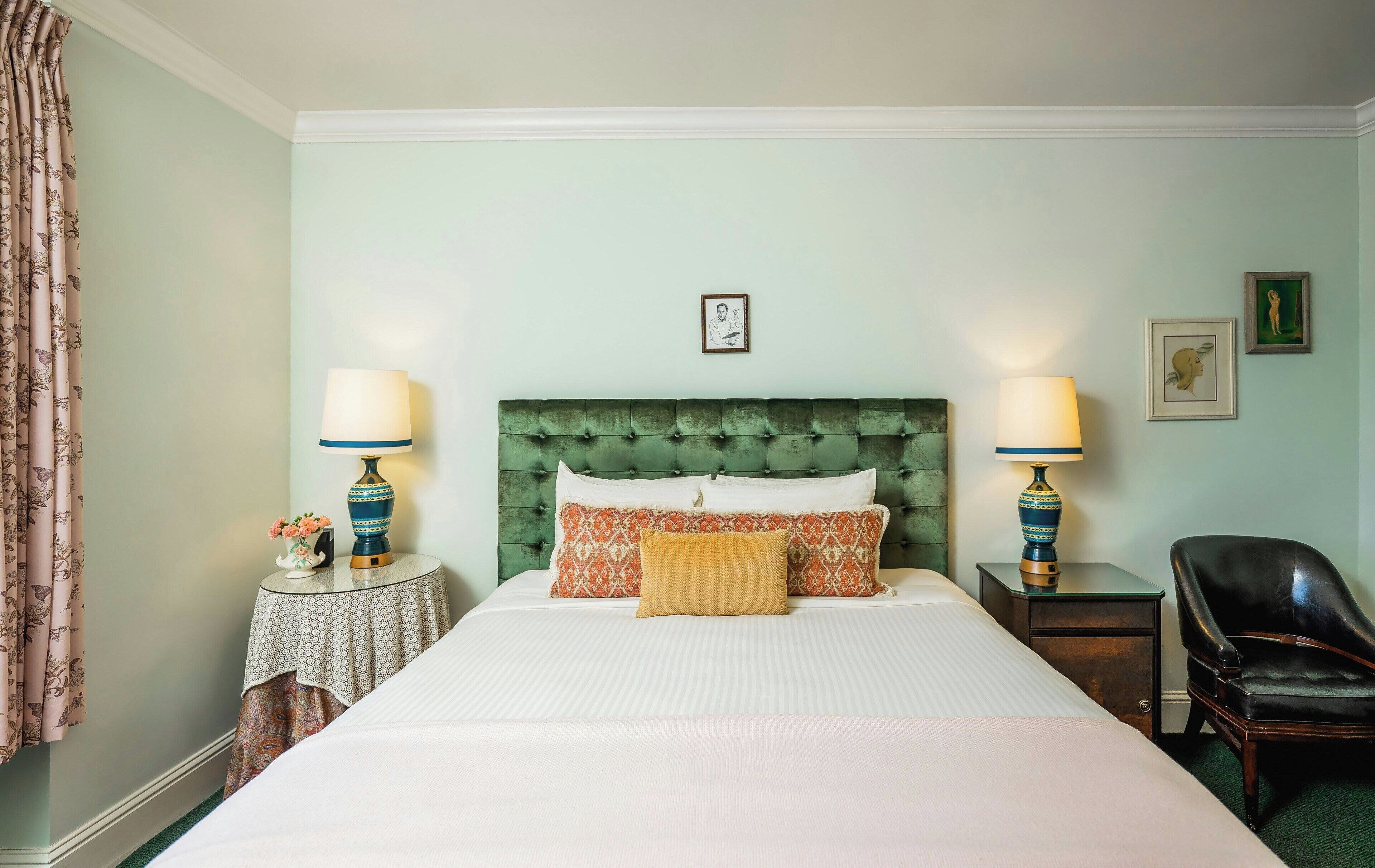 Una habitación de hotel con una cama grande, dos mesitas de noche con lámparas, una silla y una pared decorada con cuadros.