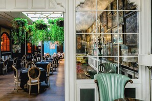 A dining area with tables and chairs, a hanging plant, and a wall with framed artwork. - The Pontchartrain Hotel (New Orleans)