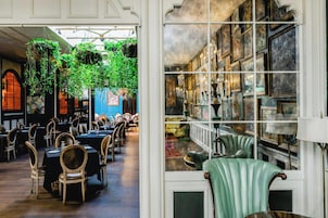 A dining area with tables and chairs, a hanging plant, and a wall with framed artwork.