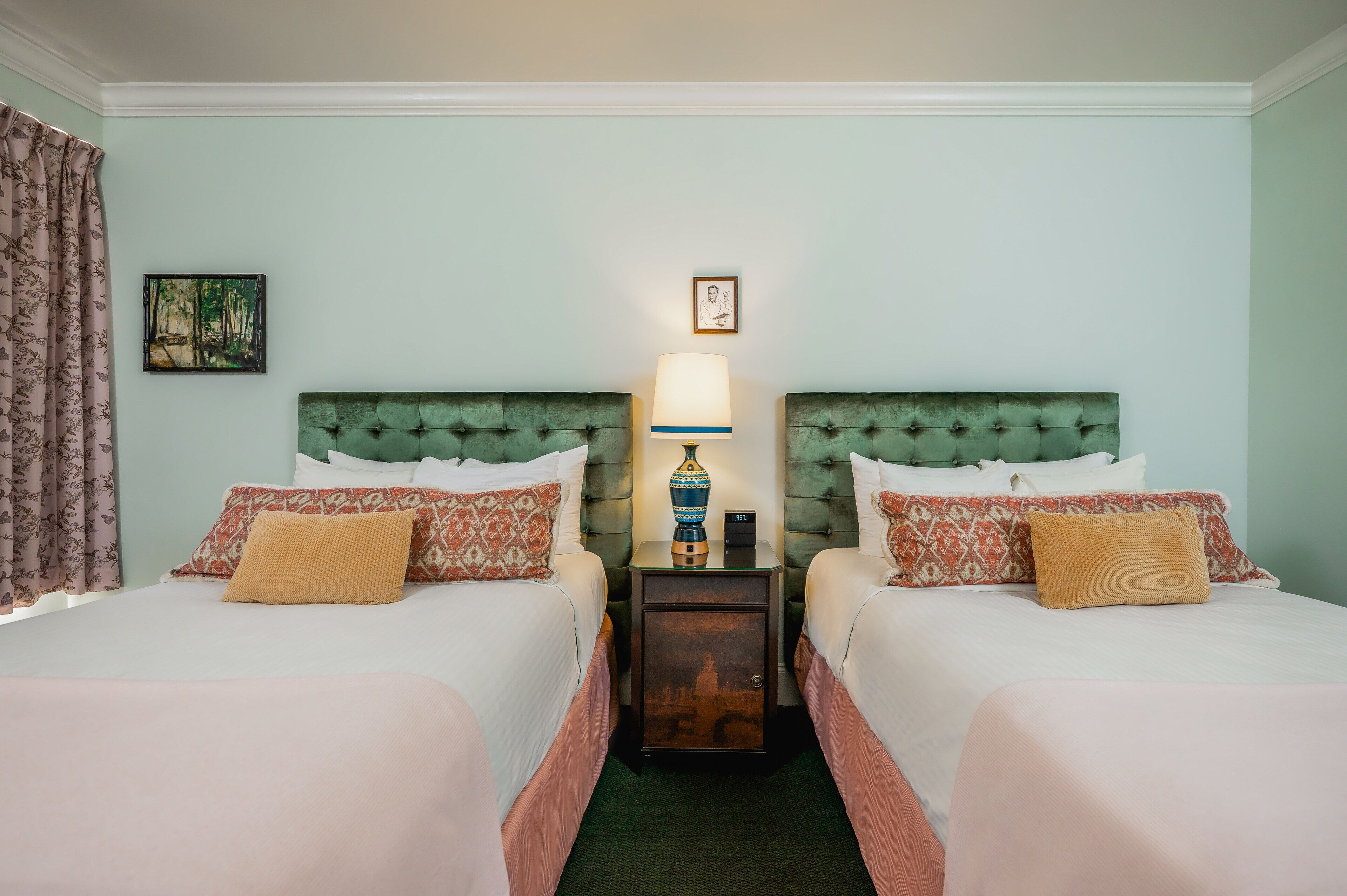 A hotel room with two beds, each with patterned pillows and a nightstand with a lamp between them.