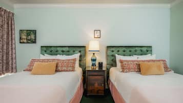 A hotel room with two beds, each with patterned pillows and a nightstand with a lamp between them.
