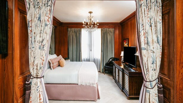 A bedroom with a large bed, wooden paneling, a chandelier, and curtains. - The Pontchartrain Hotel (New Orleans)