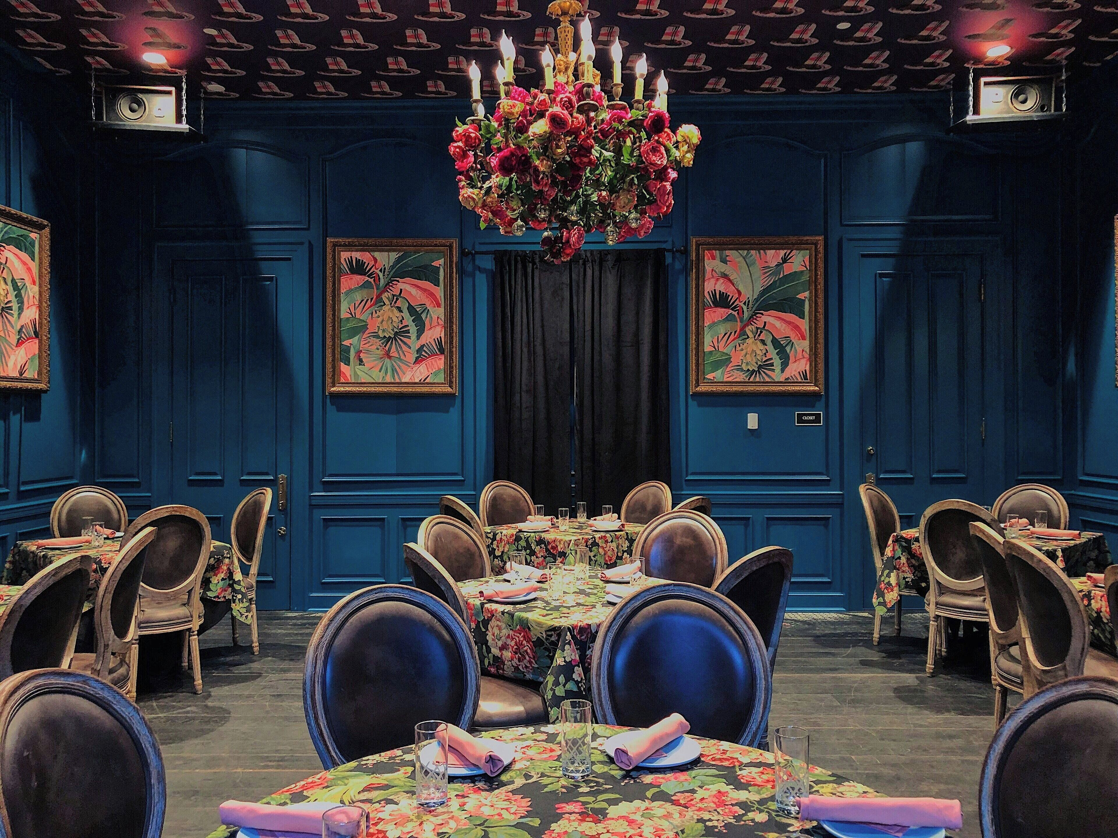 Une salle à manger élégante, agrémentée d’un lustre, de nappes à motifs floraux et d’œuvres d’art encadrées qui ornent les murs.