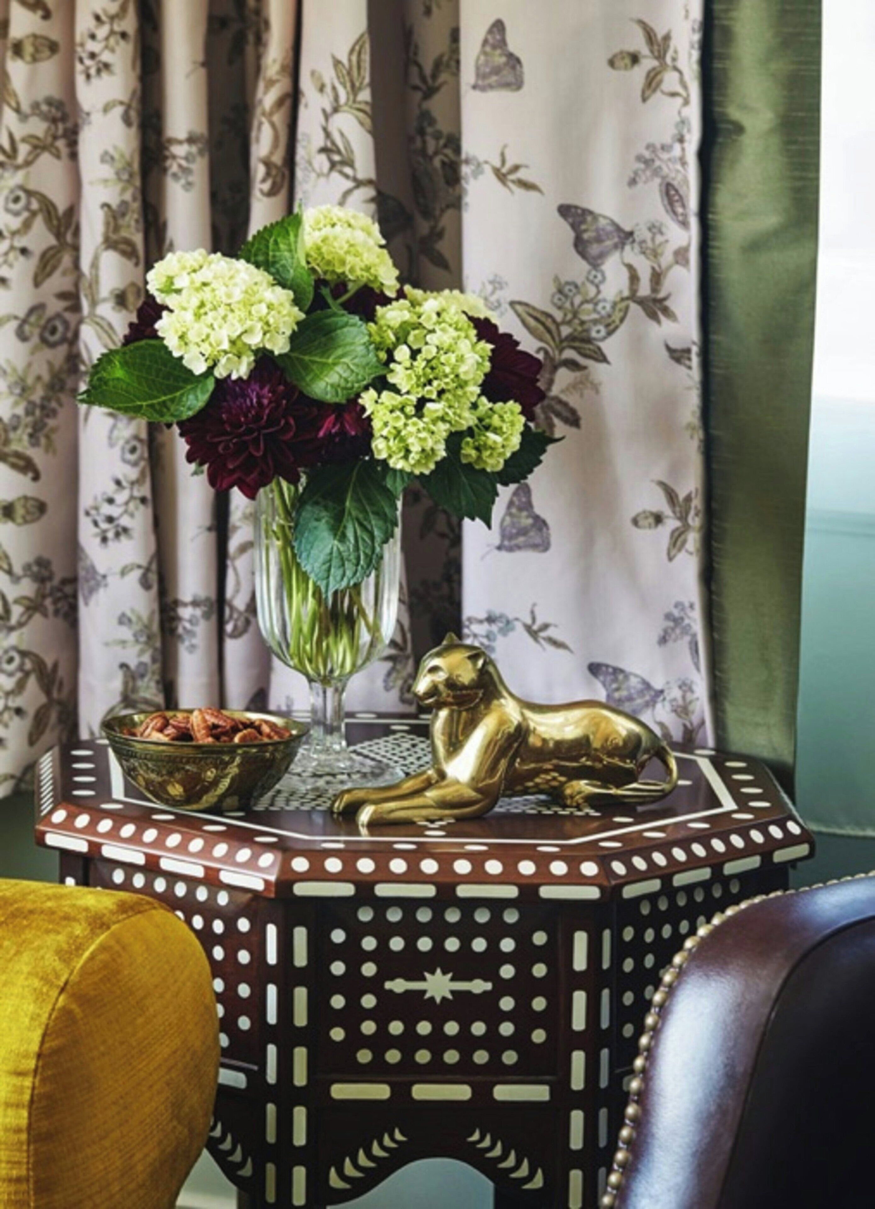 A decorative table with a vase of flowers, a bowl of nuts, and a golden cat figurine.