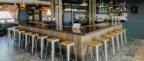Zona de bar con mostrador de madera, taburetes metálicos y lámparas colgantes.