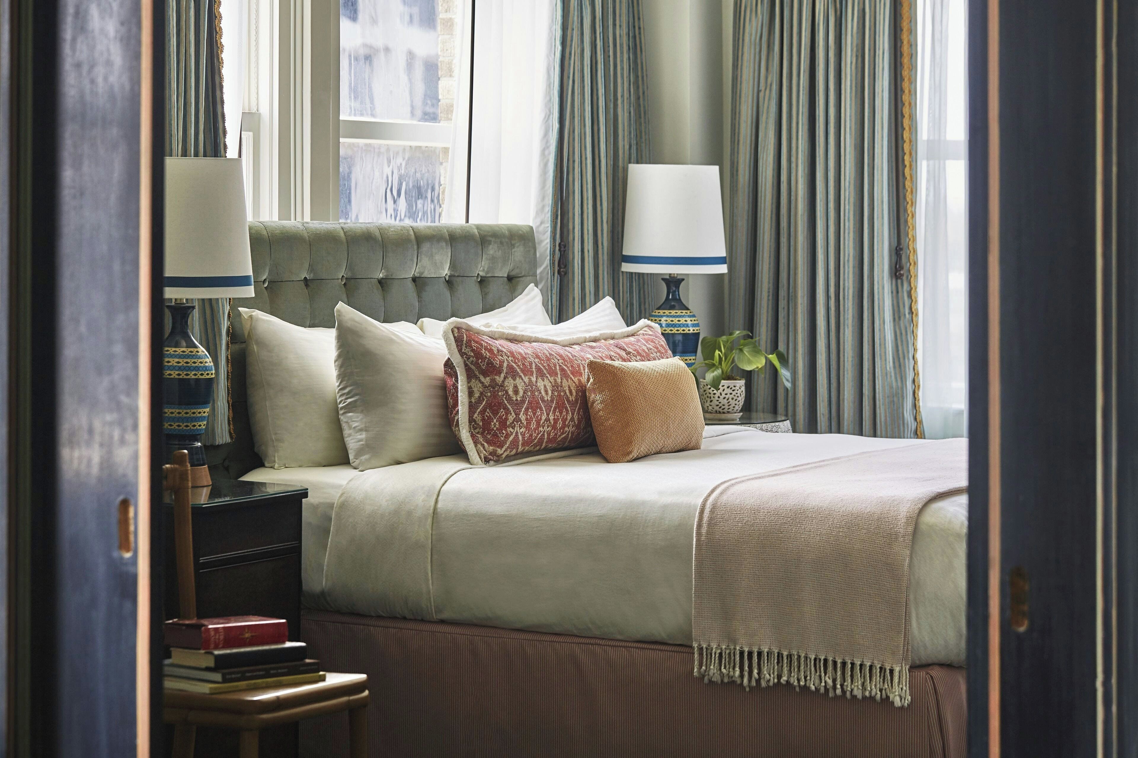 A neatly arranged bedroom with a bed, pillows, a bedside table with books, and a lamp.