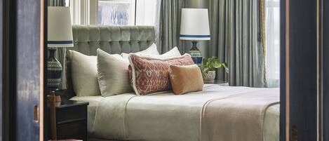 A neatly arranged bedroom with a bed, pillows, a bedside table with books, and a lamp.