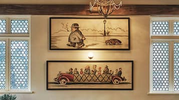 A dining area with tables and chairs, a chandelier, and two framed artworks on the wall.