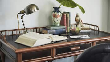 Un escritorio de madera con un libro abierto, una lámpara, un florero con una planta y una estatua de pájaro.