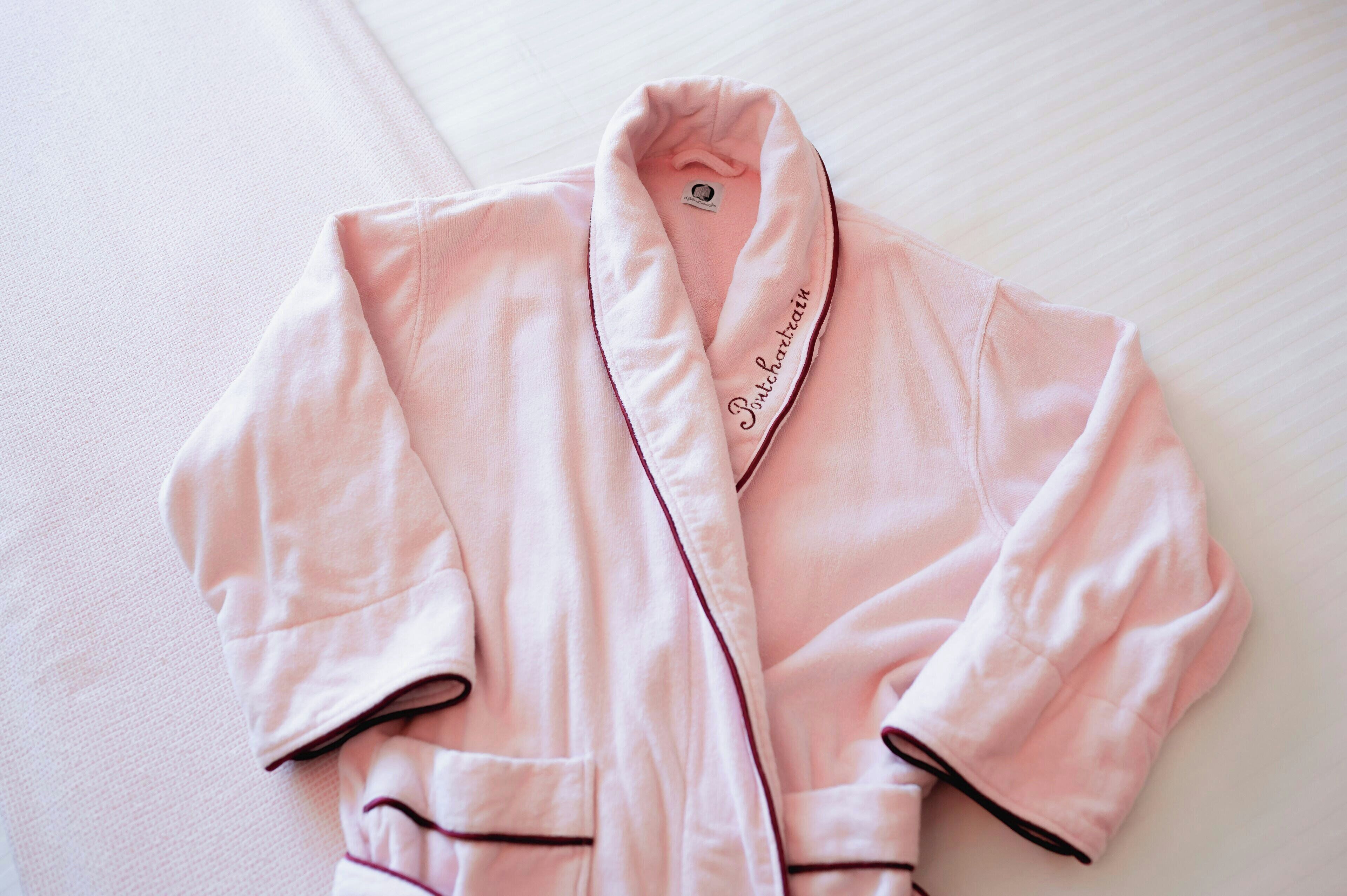 A pink robe with 'Panchatain' embroidered on it, laid on a textured surface.