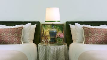 Een net opgemaakt bed met witte lakens, een kussen met dessin, een tafeltje met een bloevas en een lamp.