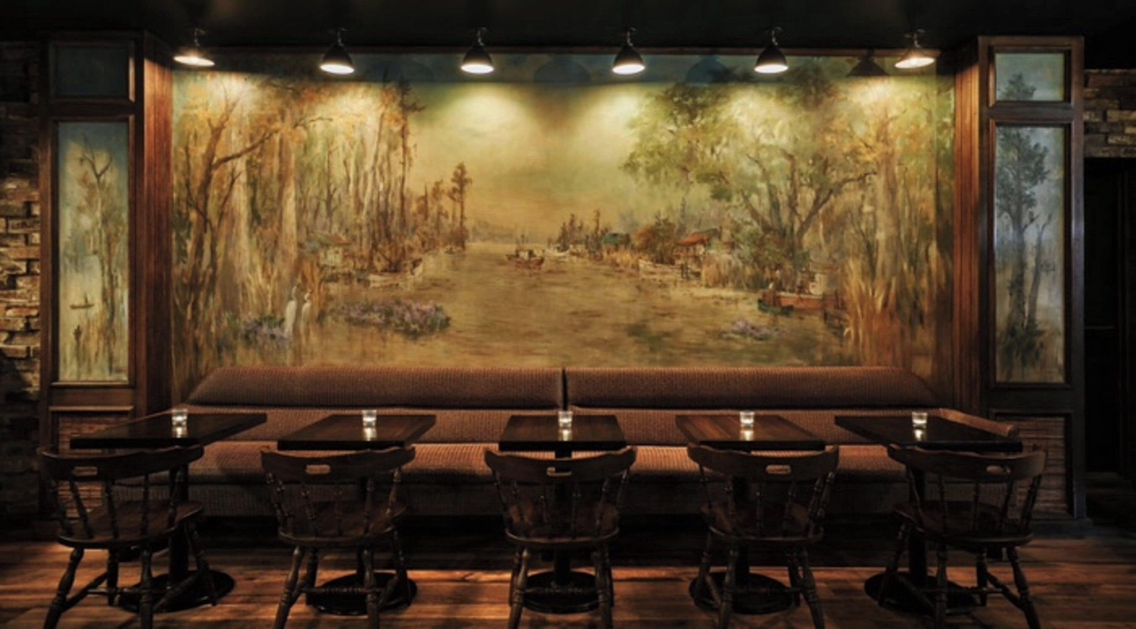 A restaurant with a large mural of a forest scene, wooden tables and chairs, and a stone wall on one side.