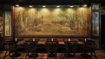 A restaurant with a large mural of a forest scene, wooden tables and chairs, and a stone wall on one side.