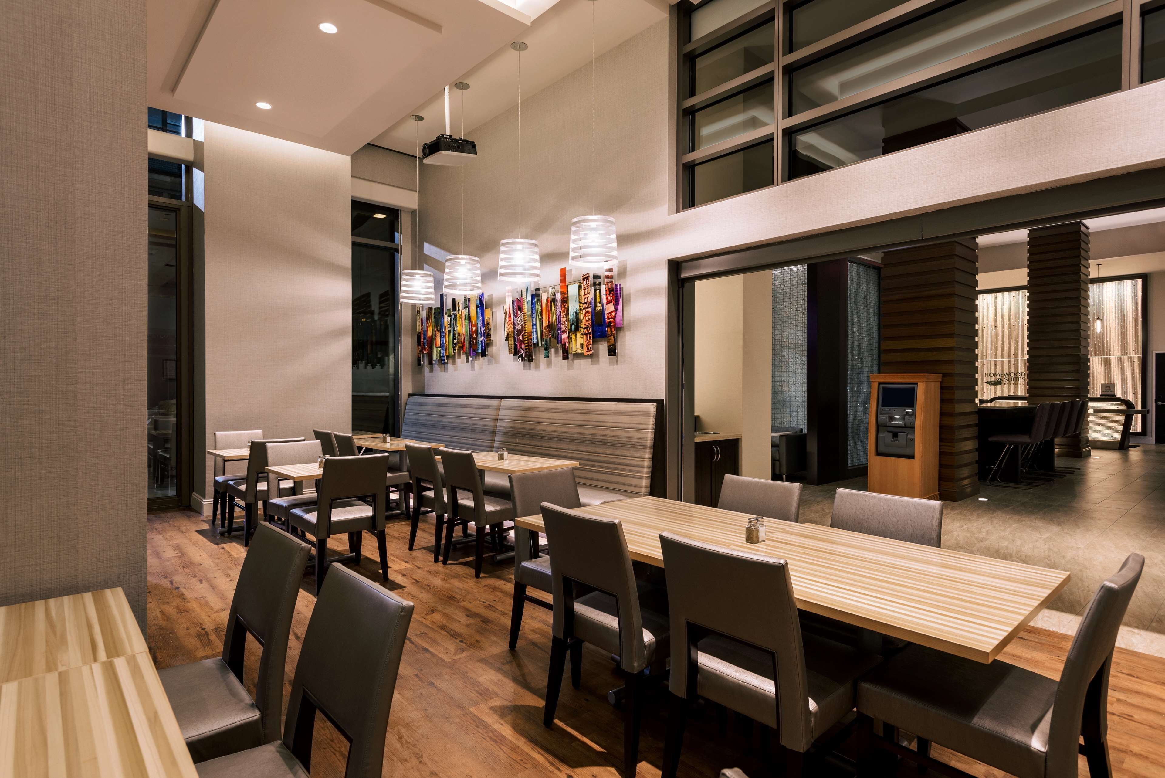A modern dining area with wooden tables and chairs, a long bench, and a wall with flags.