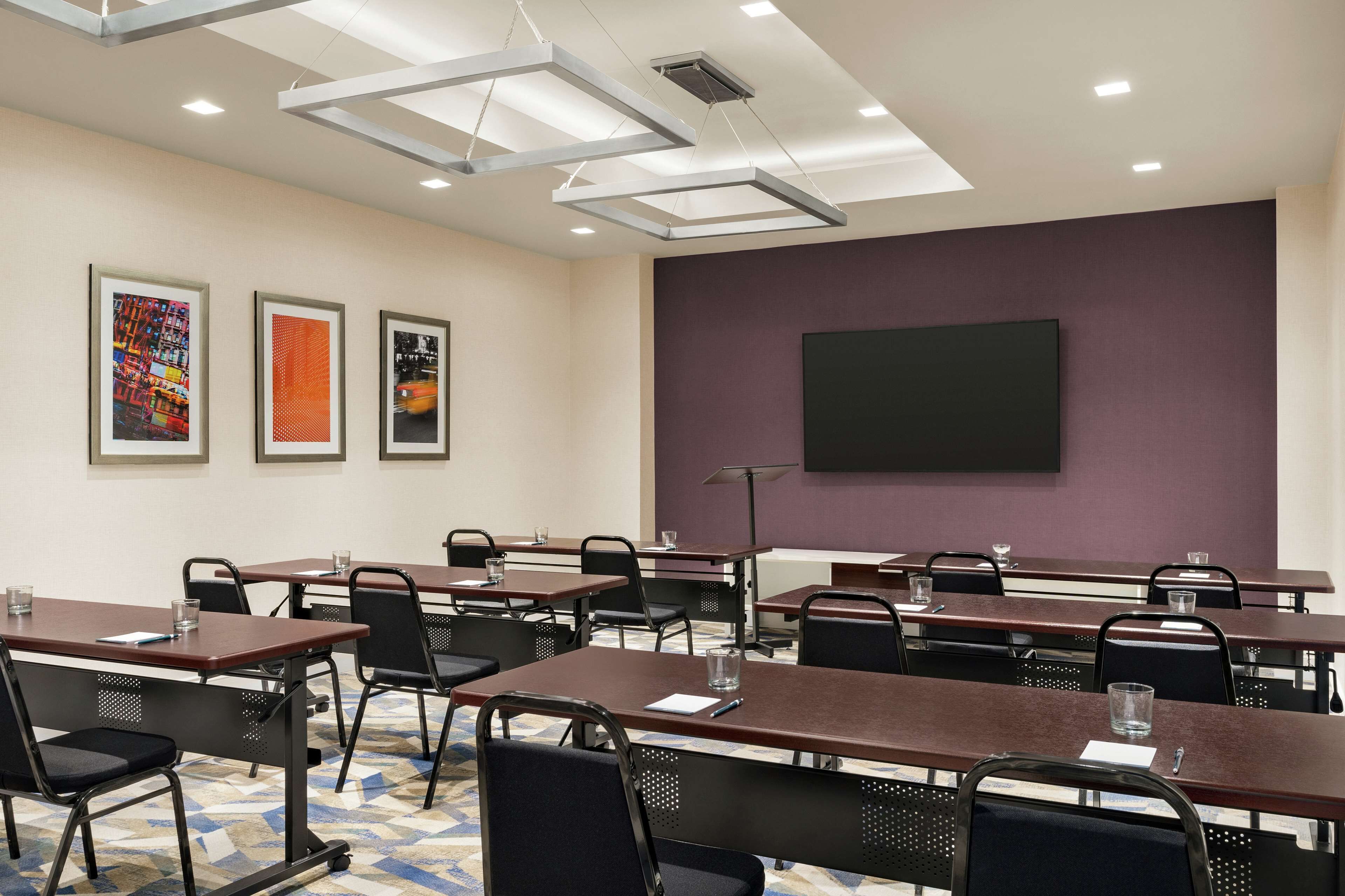 Un salón de conferencias con mesas, sillas y una pantalla grande en la pared.