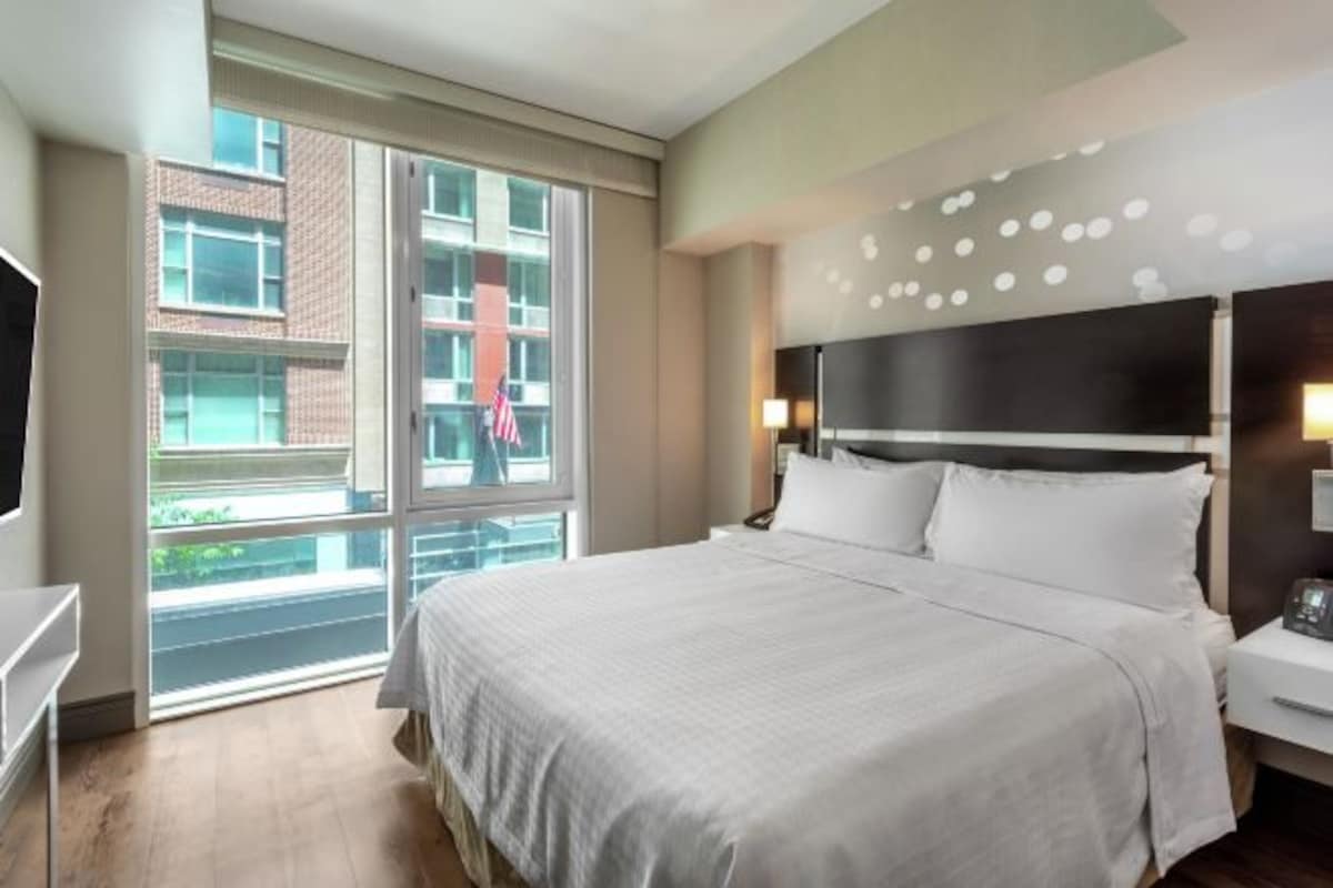 Een moderne hotelkamer met een groot bed, een televisie en een raam met uitzicht op een gebouw.
