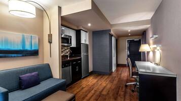 A compact living space with a kitchenette, a sofa, a desk, and a painting on the wall.