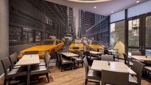 A restaurant with a mural of taxis on the wall, wooden tables and chairs, and large windows offering a view of the city.
