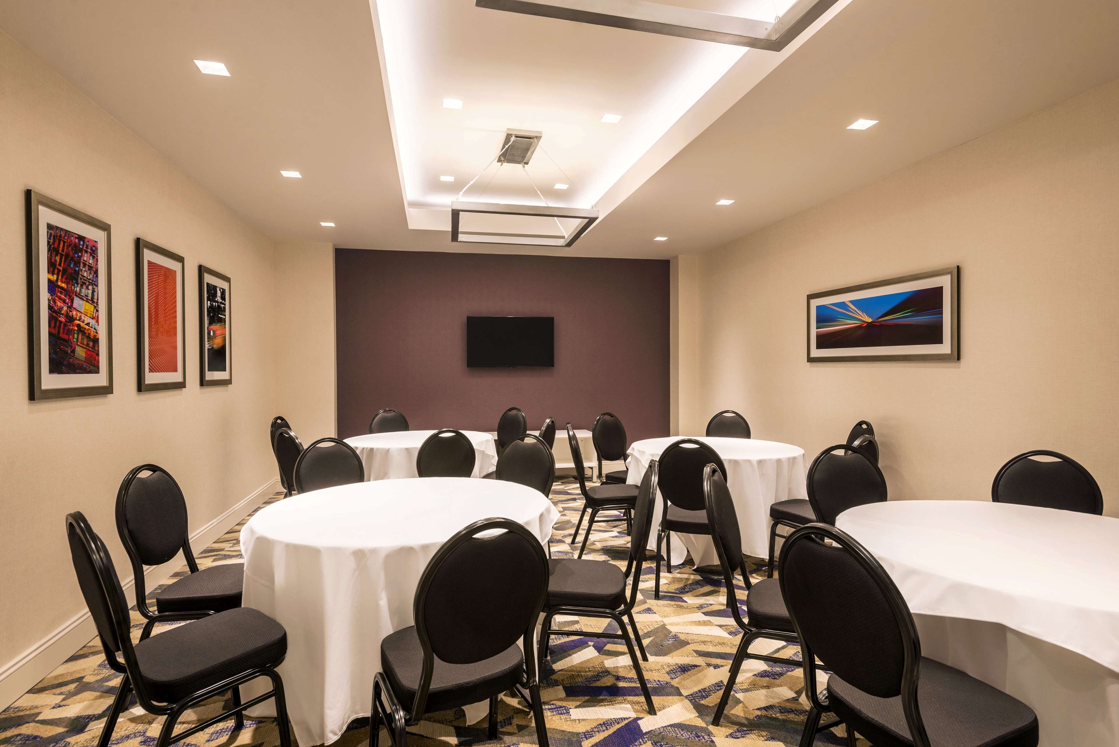 A conference room with round tables and chairs, a flat-screen TV, and framed artwork on the walls.