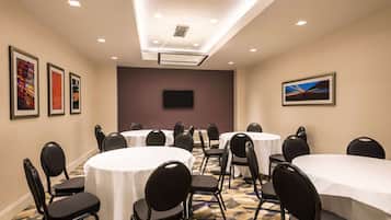 A conference room with round tables and chairs, a flat-screen TV, and framed artwork on the walls.