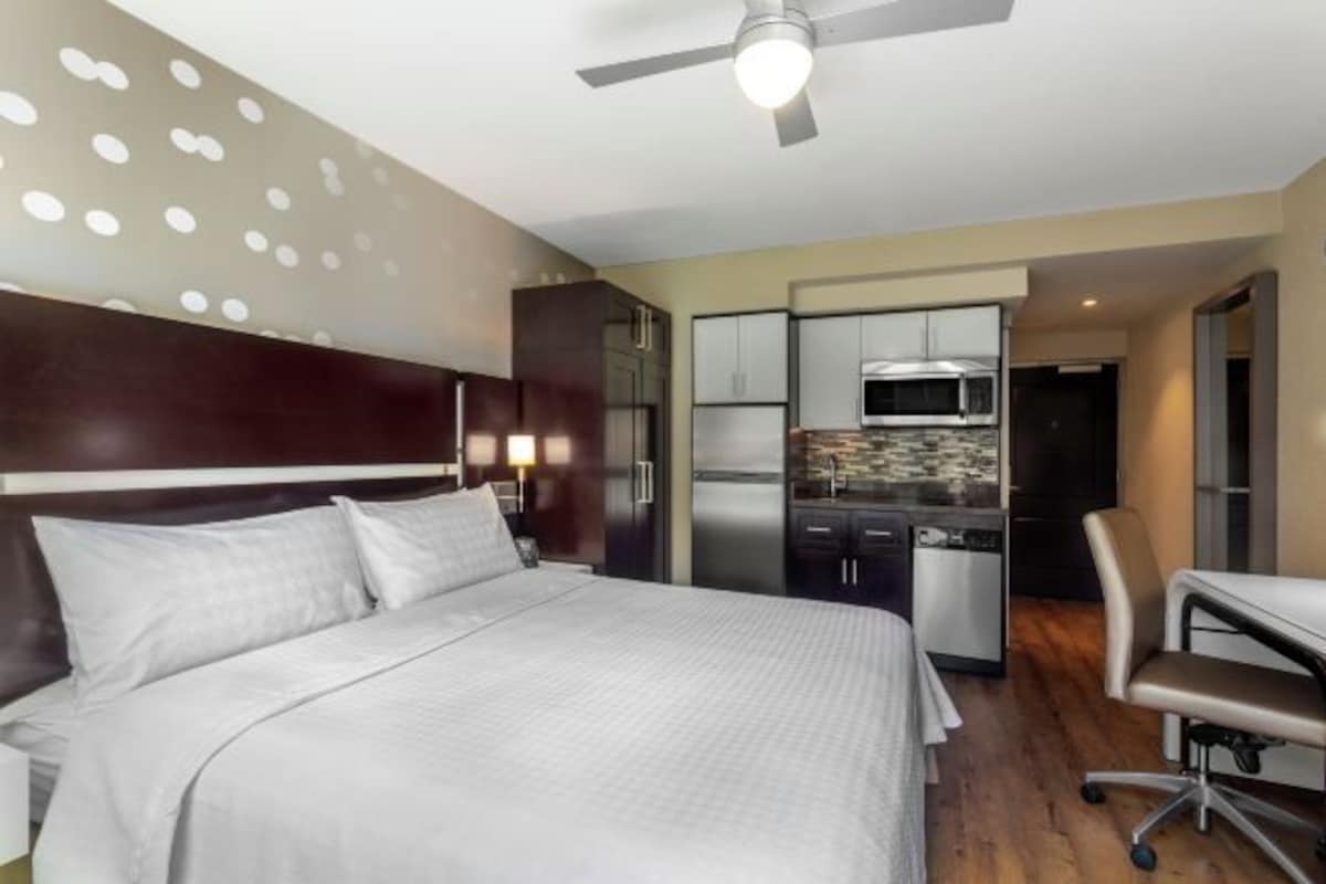 Hotelkamer met een bed, bureau, stoel, kitchenette en plafondventilator.