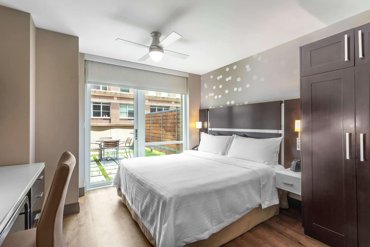 Ein Hotelzimmer mit Bett, Schreibtisch, Stuhl, Kleiderschrank, Deckenventilator und Blick nach außen.