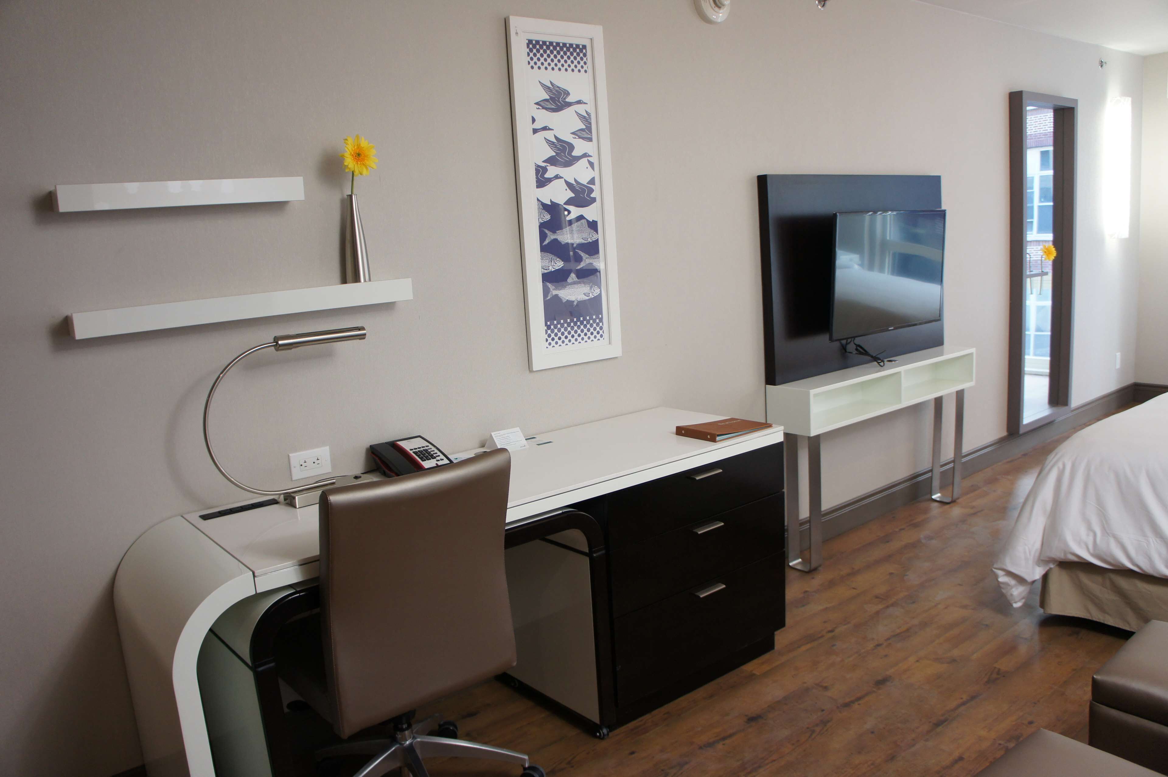 A hotel room with a desk, chair, TV, and a bed.