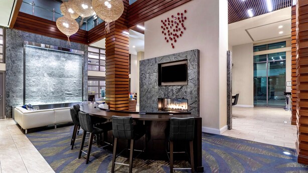 A modern bar area with a marble countertop, two bar stools, a fireplace, and a large TV screen.
