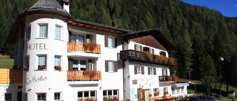 A hotel with a balcony, a sign reading "HOTEL," and a view of a forested mountain.