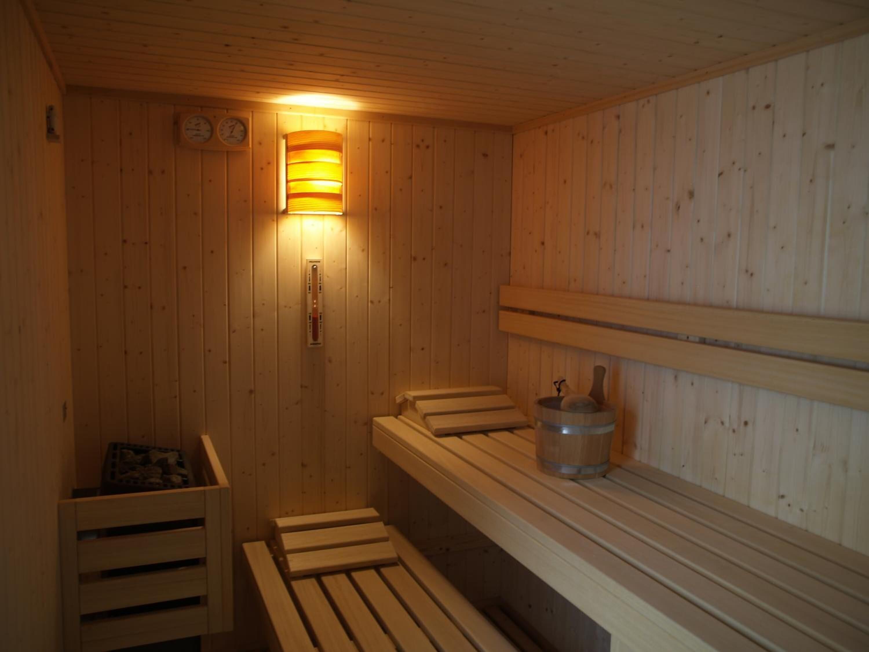 A wooden sauna with benches, a wall-mounted heater, and a clock.