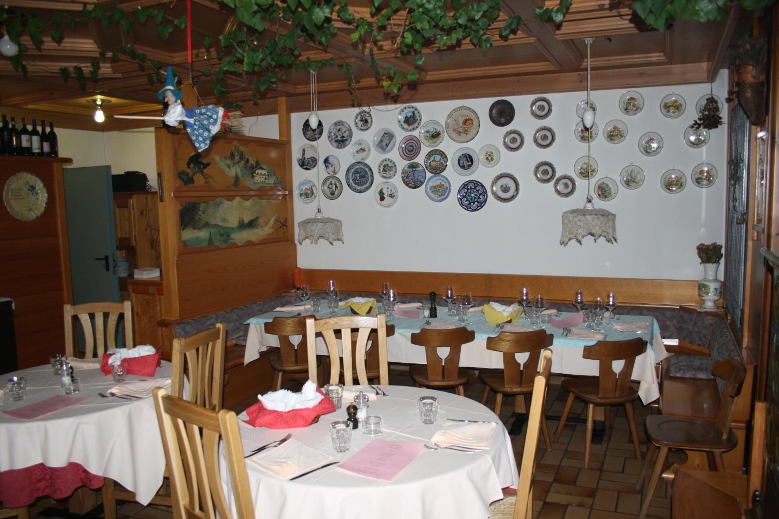 Un ristorante con diversi tavoli rotondi, sedie in legno e un muro decorato con diverse piastre.