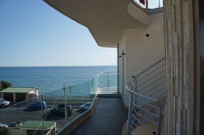 A balcony with a view of the sea, a parking area with cars, and a building facade with a railing. - L'Approdo (Anzio)