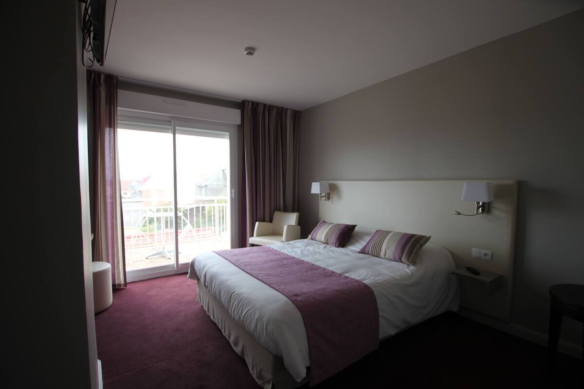 A hotel room with a large bed, a balcony, and a view of the outside.