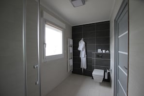 Un baño moderno con mampara de vidrio, inodoro blanco y pared de azulejos oscuros.
